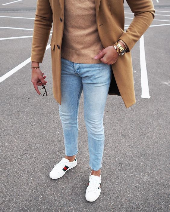 Hombre usando zapatillas, jeans, abrigo y sweater camel.
